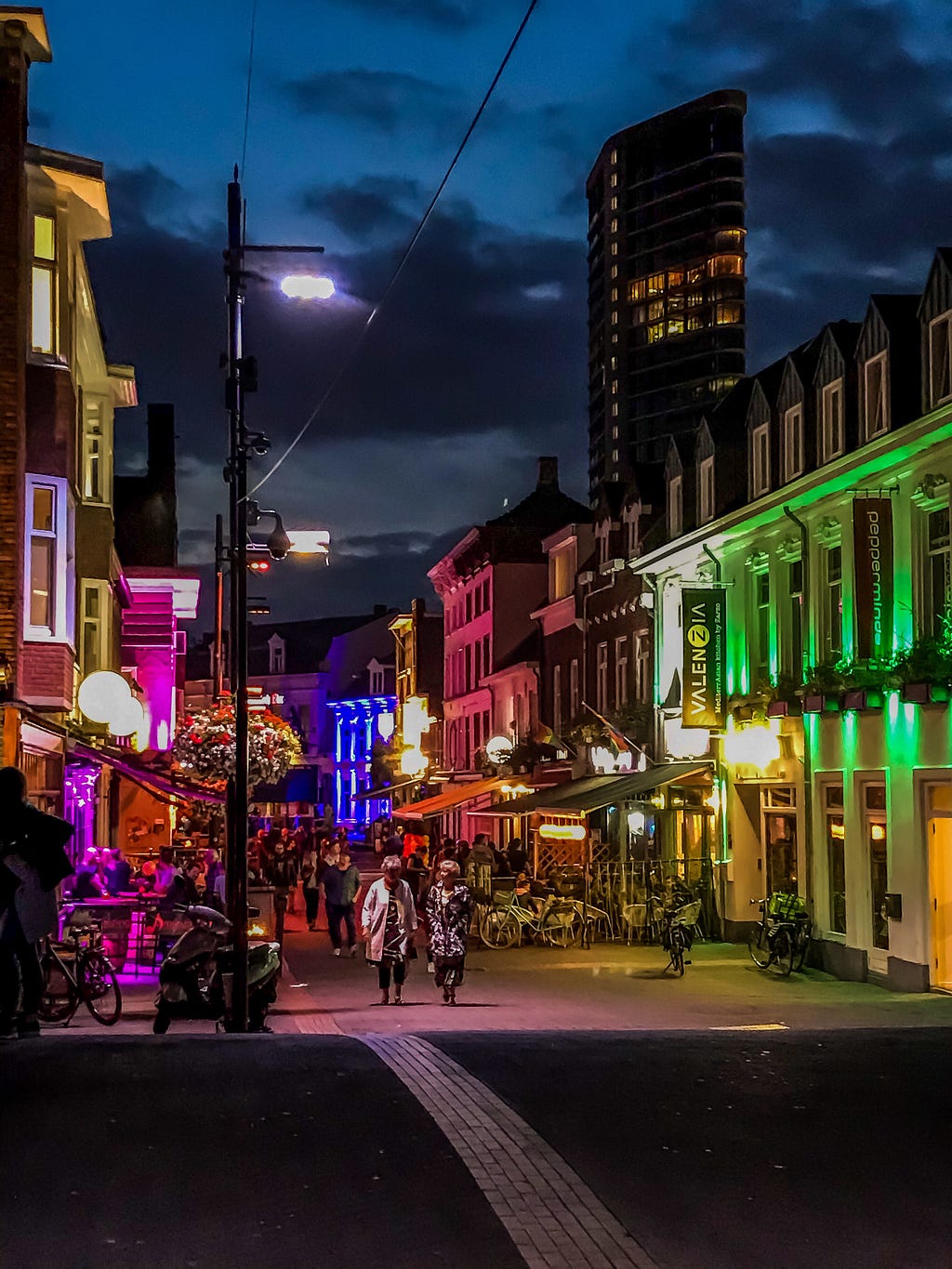 The photo displays Sratumseind Street in Eindhoven, The Netherlands at night with colourful lights and pedestrians