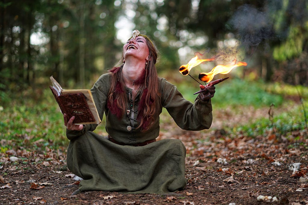 Which apparently looks something like a young female holding an old-looking book juggling fire in the forest somewhere?