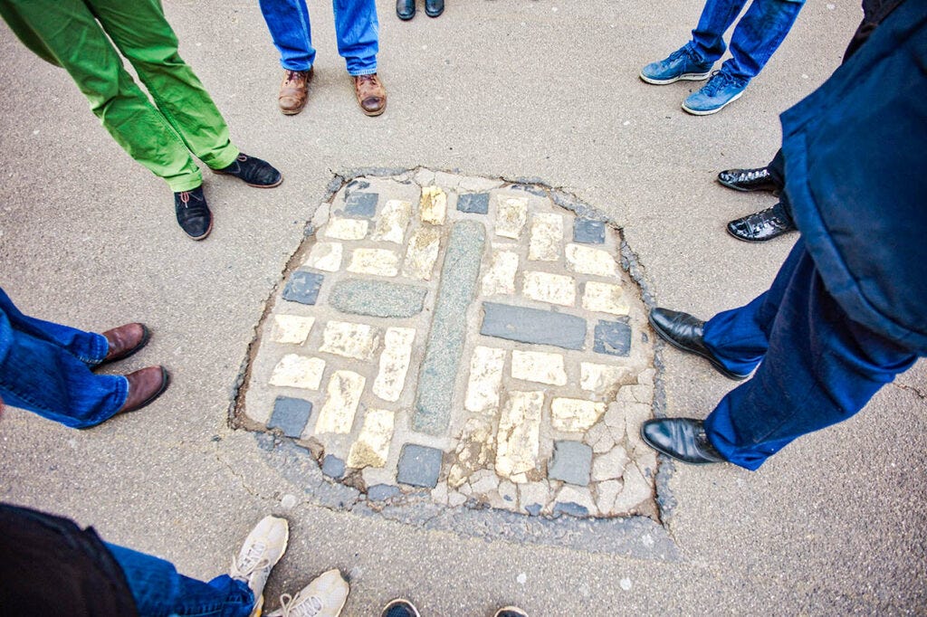 9 people standing in a circle around an exposed section of road, you can only see the peolpes legs and feet