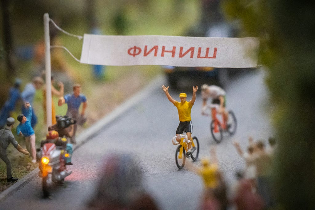 Cyclist crossing the finish line, with both hands raised in victory.