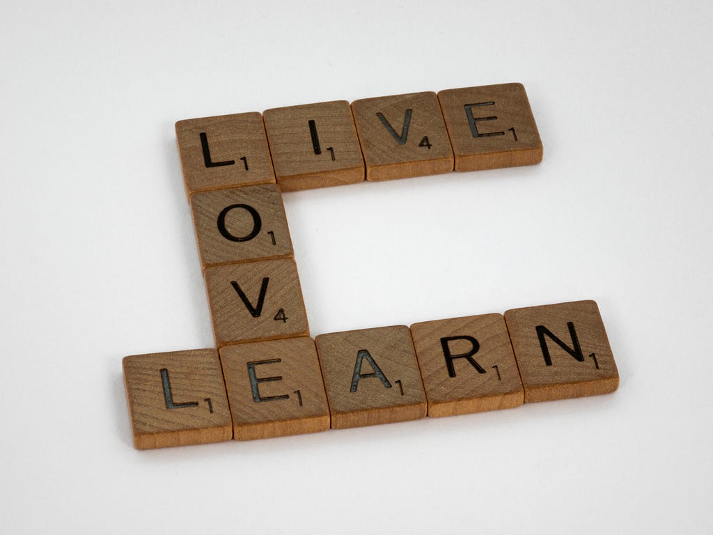 Brown wooden squares with black capital letters on them and a small number, one on each square, arranged to say “Live, Love, Learn”