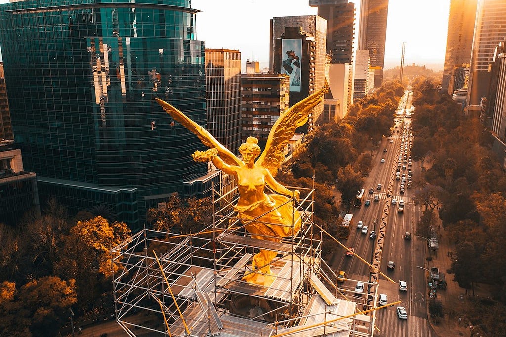 Gold statue of a winged woman, surrounded by scaffolding and above a busy freeway