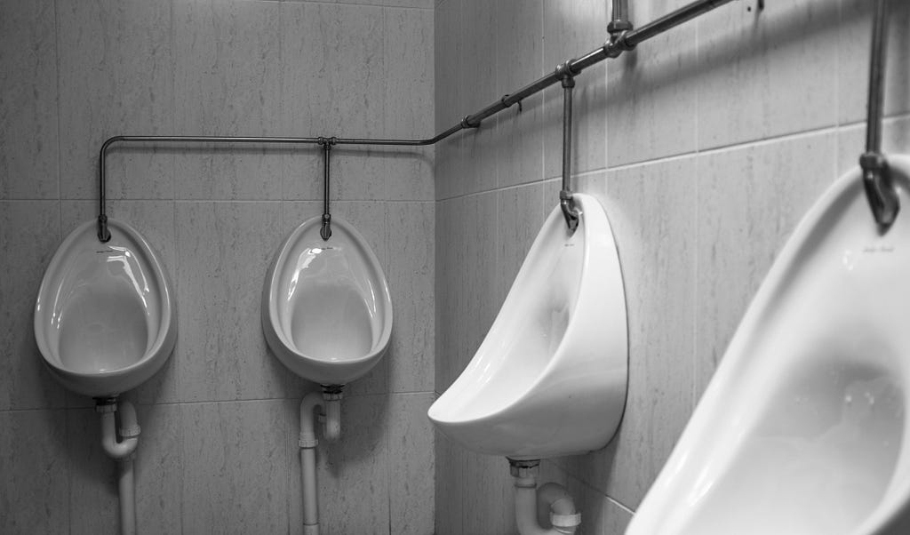 Black and white photo of four basic, wall-mounted, urinals