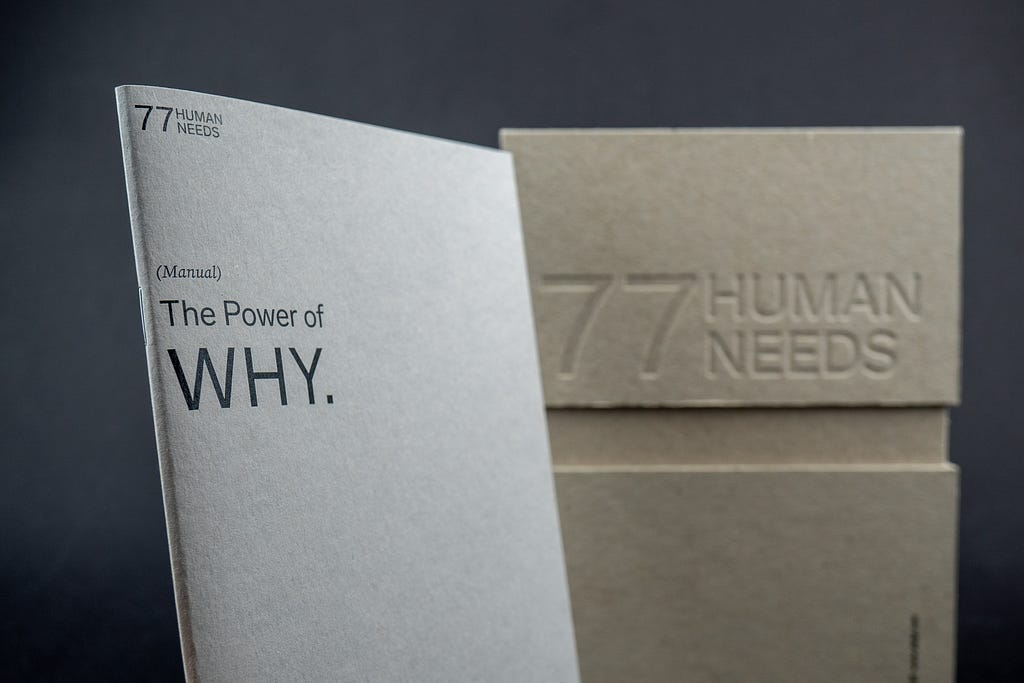 The image shows a book titled “The Power of Why”. The book is sitting on a table next to a cardboard box. The book is open to a page with the text “77 WEE PHUMAN”. The box has the text “The Power of WHY. 77HUMAN NEEDS”.
 
 The image is simple and minimalist, with a focus on the book and the text. The colors are muted, with the dominant colors being white, black, and brown. The overall impression is one of calm and introspection.
