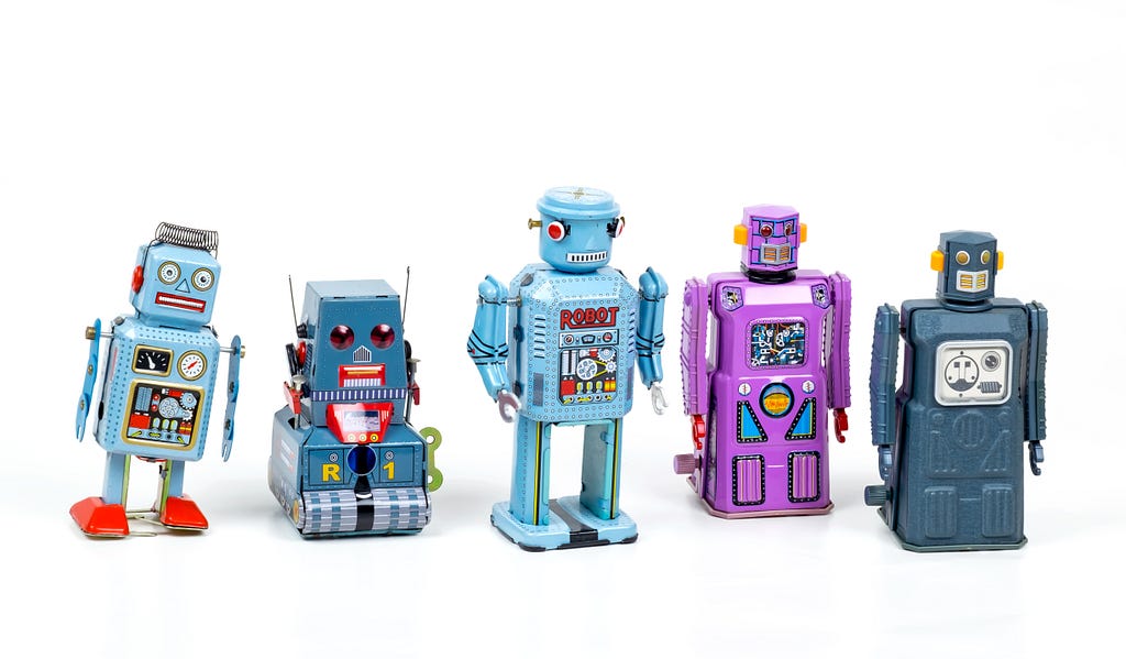 Small robot toys in a line, on a white bacckground, looking stylized and cartoonish in colors ranging from blue-gray to purple