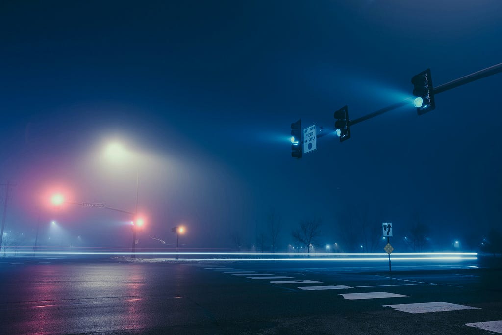 a foggy intersection of streets with red and green traffic lights and a crosswalk