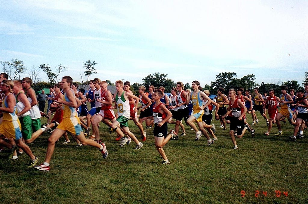 Luke Brenneman as a teen, center in red and black, running amongst many other teens, but very clearly smaller in stature.