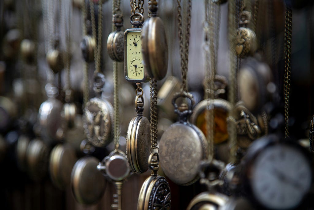 A display of dozens of older pocket watches hang from a wall, filling the frame.