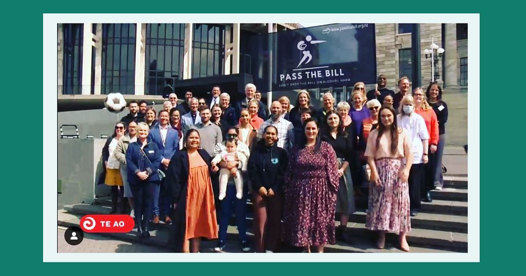 Image description: A group of people from Hāpai Te Hauora, Alcohol Healthwatch and supporters standing on the steps of Parliament smiling at the camera during their petition delivery. In the back is a large banner with the text “Pass the Bill”