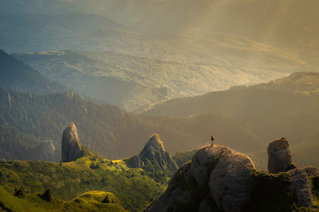 Far away picture of majestic green mountains with a human standing on one of them