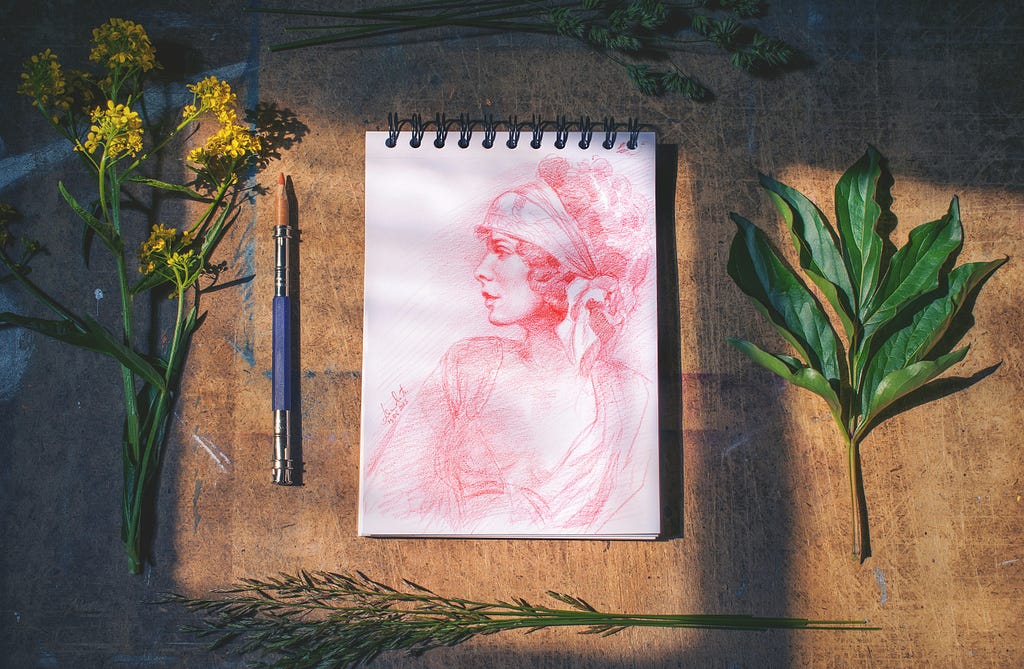 a sketch pad on a table, a sketch of a lady wearing a headscarf.