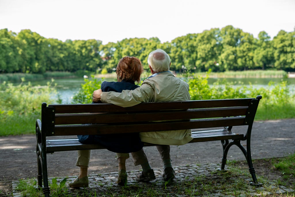 An elderly couple sits on a park bench.