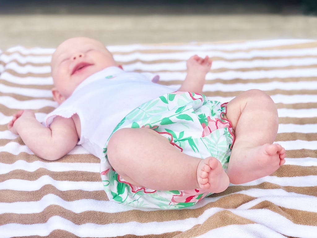 Bebê sorrindo e deitado sob uma toalha de piscina.