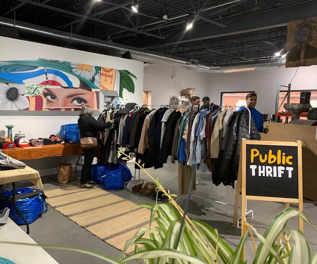 A Public Thrift Pop-Up event with racks of thrifted clothing and tables with objects for sale.