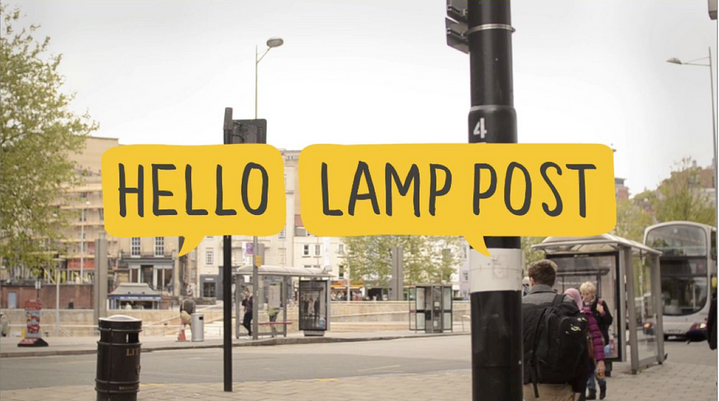 A picture of a street in Bristol with two bright sketched yellow speech bubbles superimposed which read ‘hello lamp post’