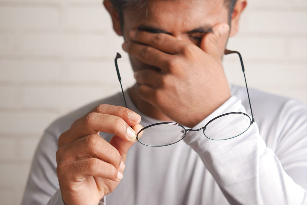 A man removes his glasses and covers his face in frustration.