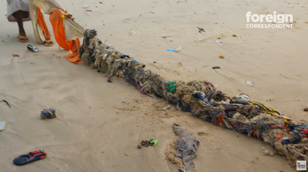 person on beach dragging a tangled assortment of clothes