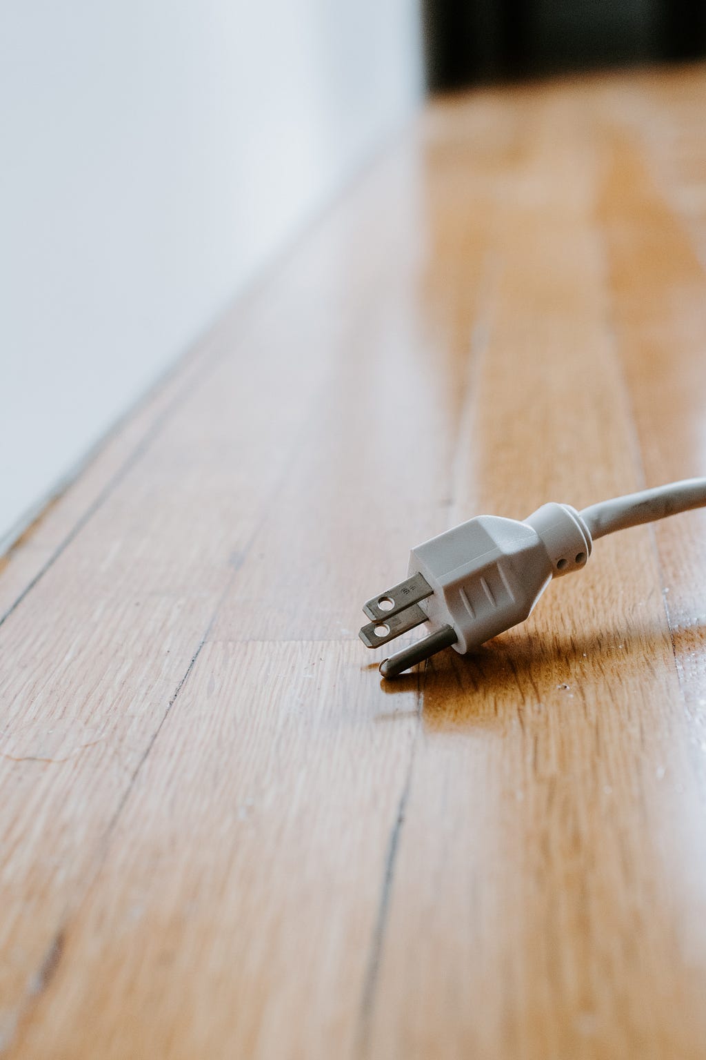 A photo of a white outlet unplugged on a tan wooden floor.