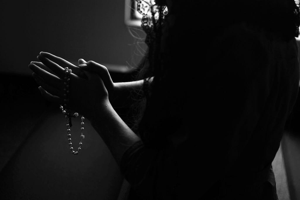 A woman holding the rosary in her hands and praying