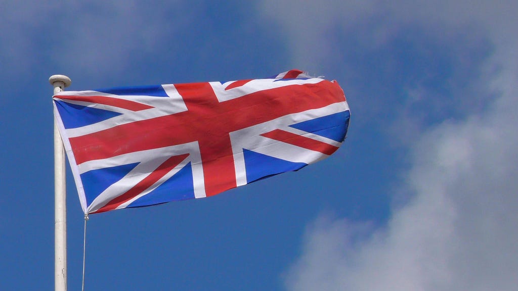 The Union Jack flying on a flagpole on a blue sky.
