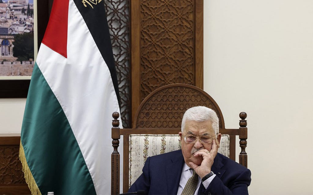 A picture showing Mahmoud Abbas, the President of the State of Palestine, sitting on a decorated armchair with the Palestinian flag visible in the background.