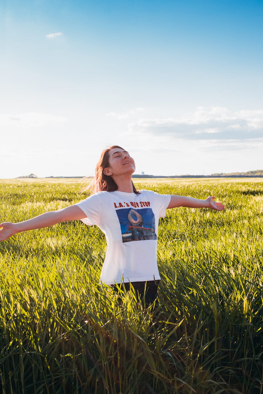 A joyful woman spreads out her arms in a grassy field.