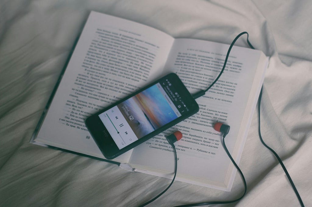 book with a phone and earbuds on top on a white sheet