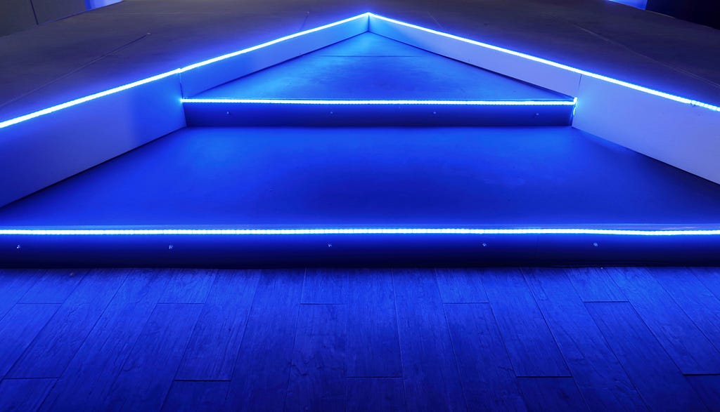 A blue neon light covered stairway converging on the horizon