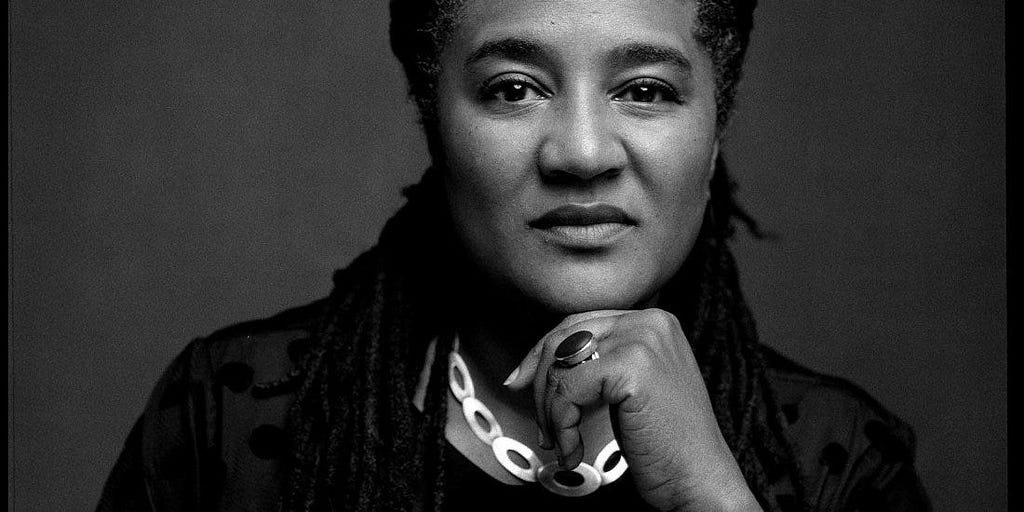 A black and white photo of a woman with dreadlocks and a large linked necklace.