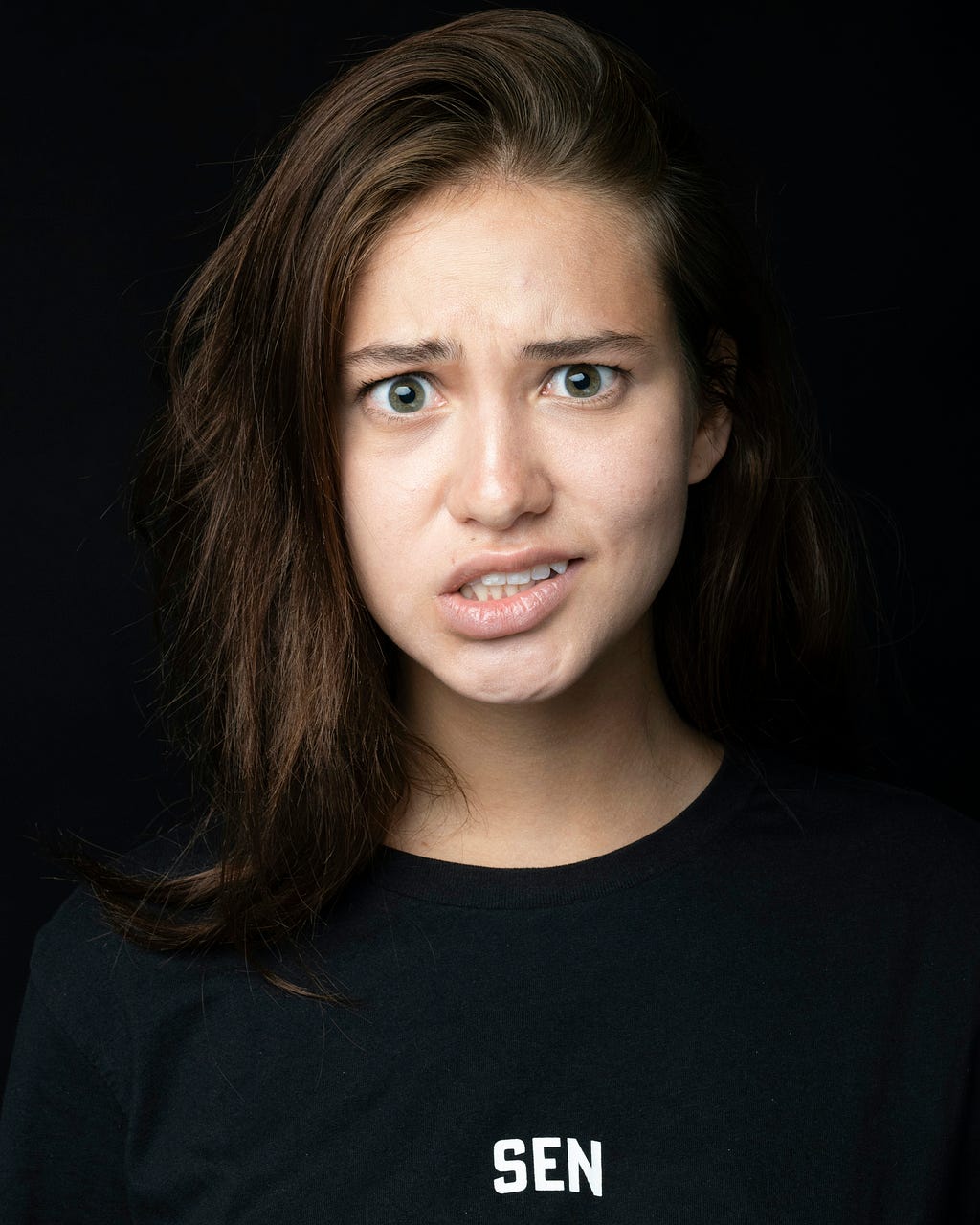 A 20-something year old Caucasian girl with brown hair, wearing a black shirt and staring straight ahead with a confused look on her face.