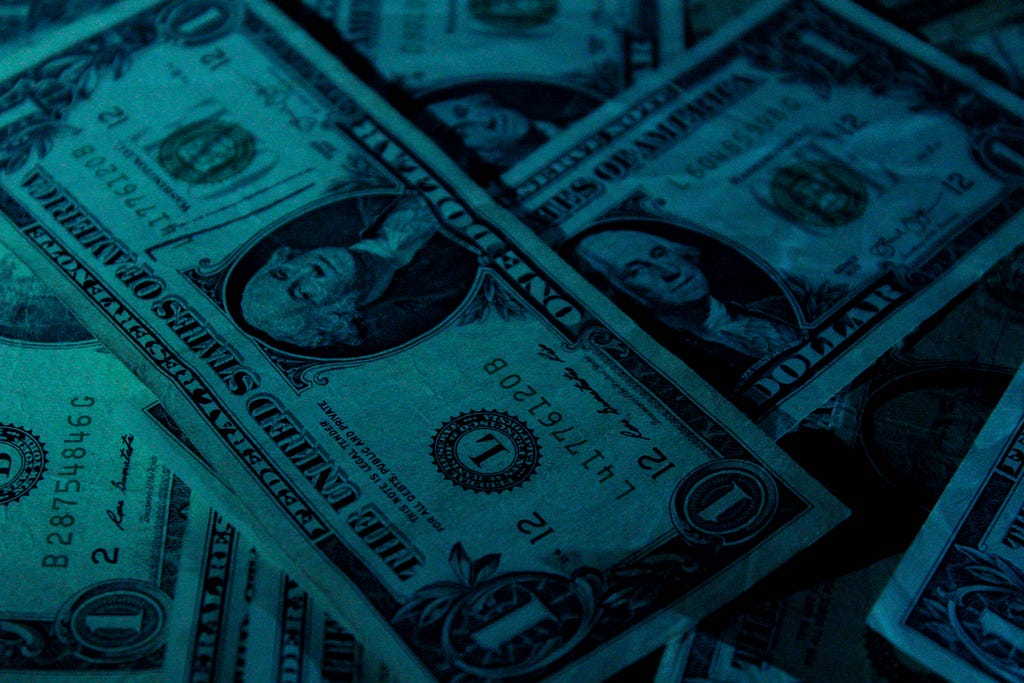 A blue-toned photo of a pile of American one-dollar bills.