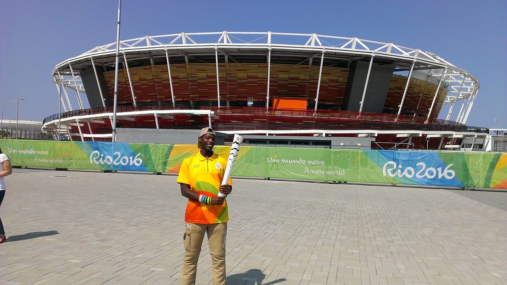 Sydney holding the Olympic torch by the Tennis stadium at the Olympic village in Rio de Janeiro