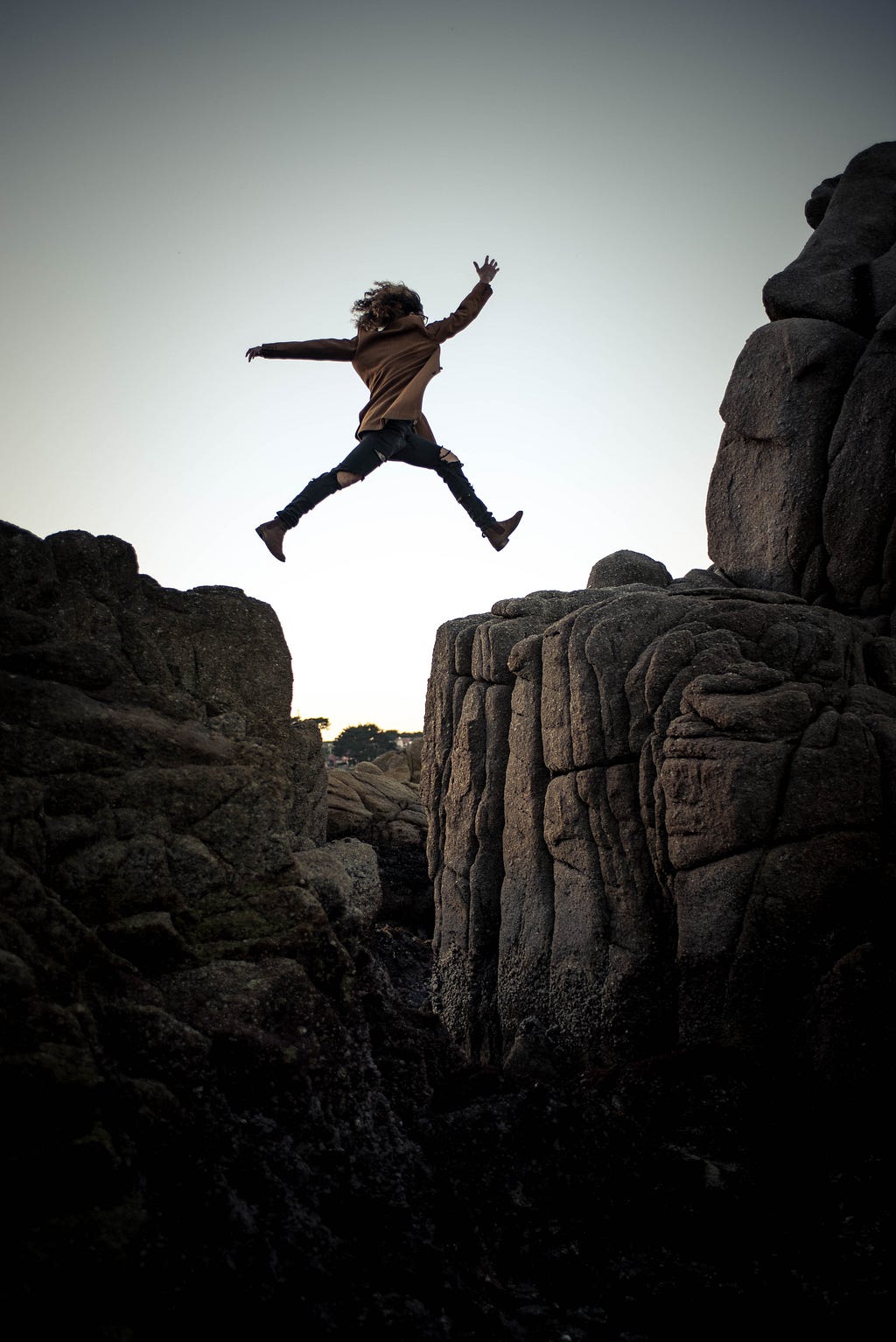 A girl jumping over the crevice between two big rocks.
