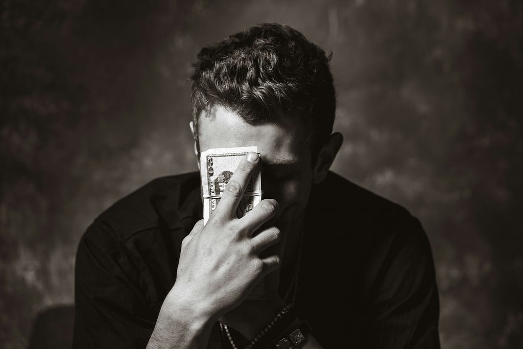 Black and white photo of a human with their eyes closed and holding a wad of cash up to their forehead.