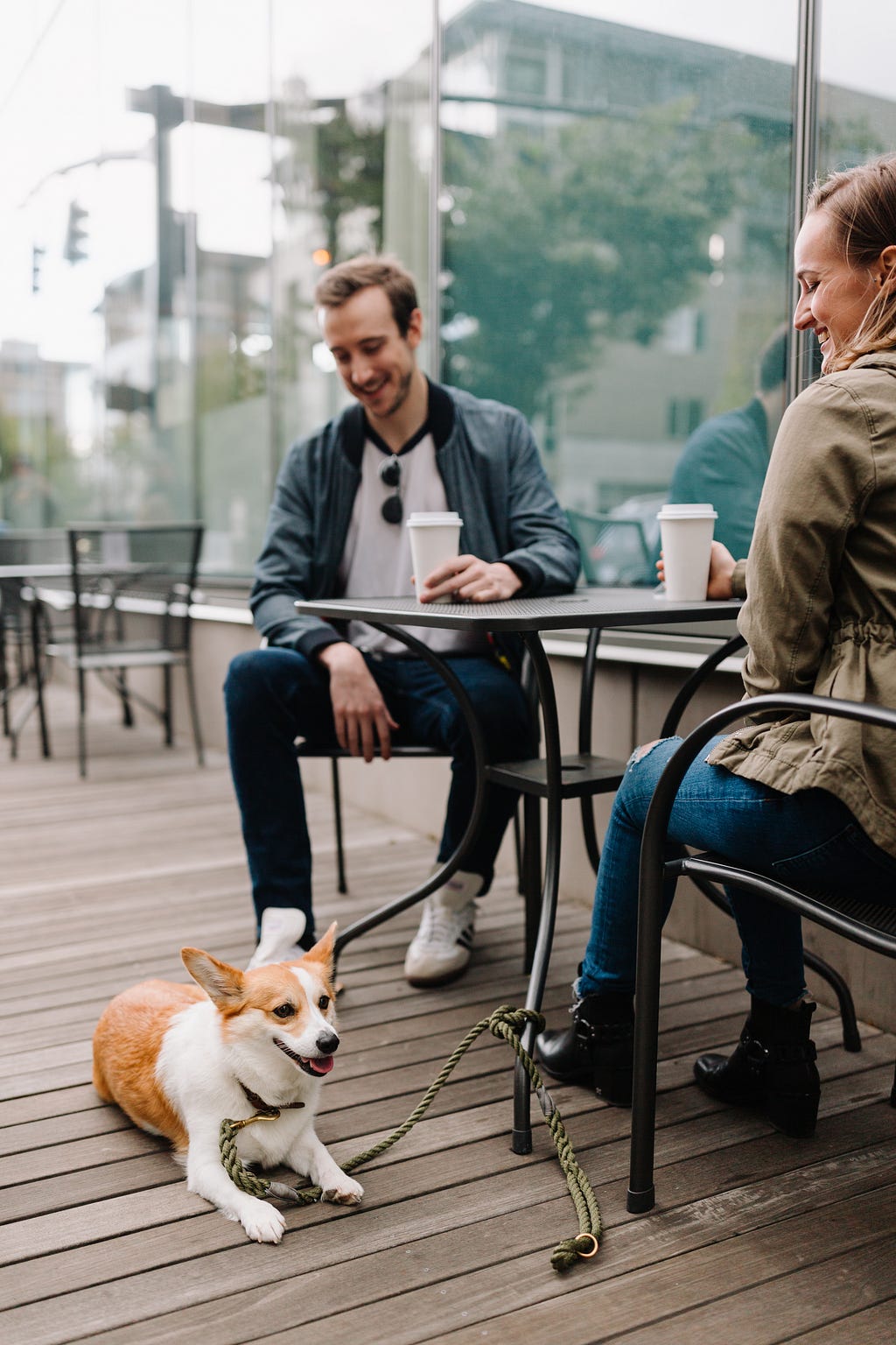 man and woman drinking coffee and looking at their pet corgi dog.