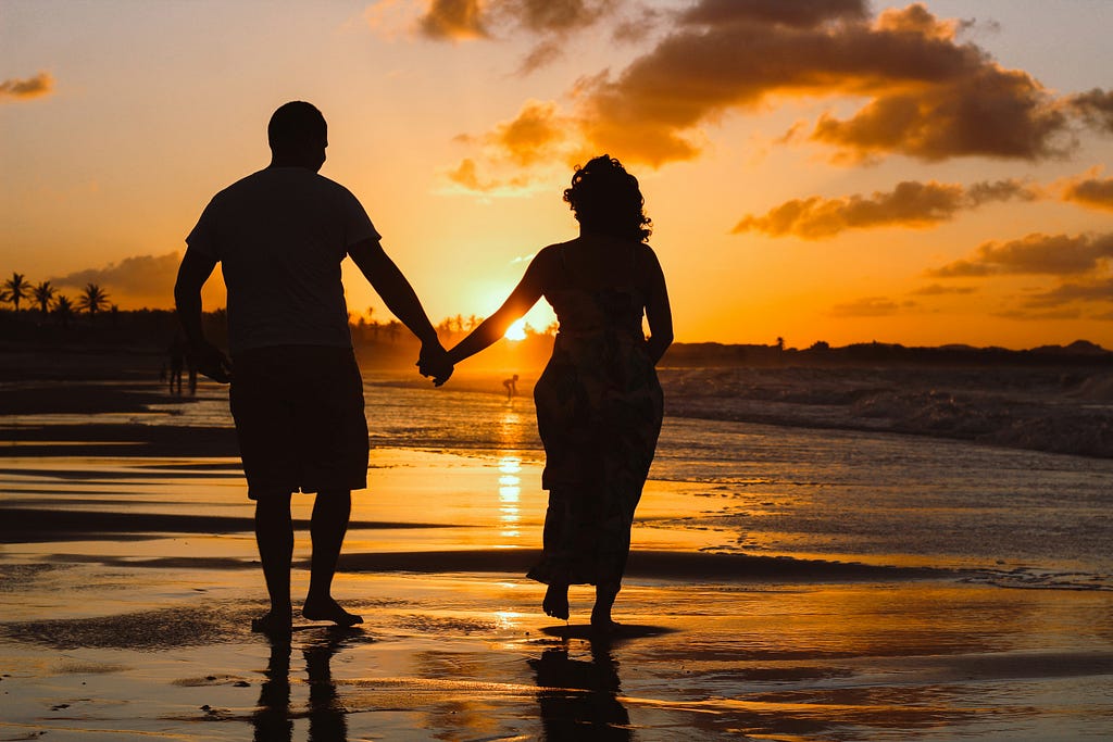 A couple walks hand in hand along the shore of the beach
