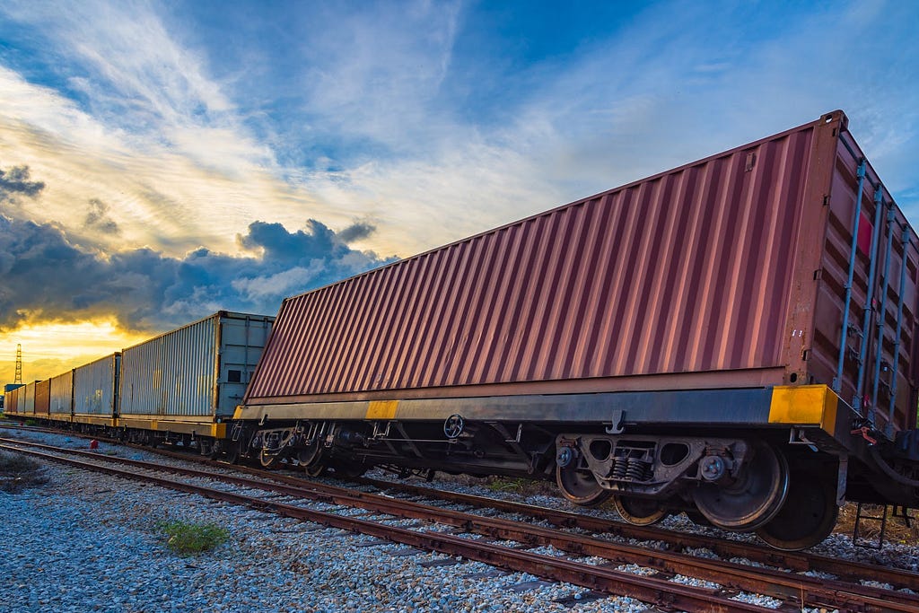 Railroad track with maroon shipping container slightly tipped over on its side