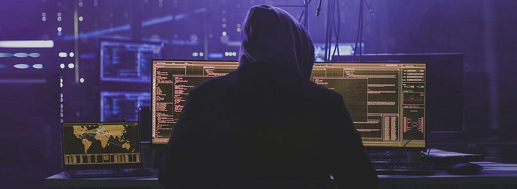 Hacker em uma sala escura olhando para três monitores