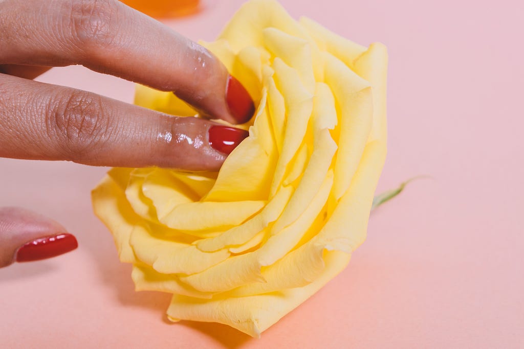 Image of lubricated fingers with red nails touching a yellow rose to indicate a sexual act
