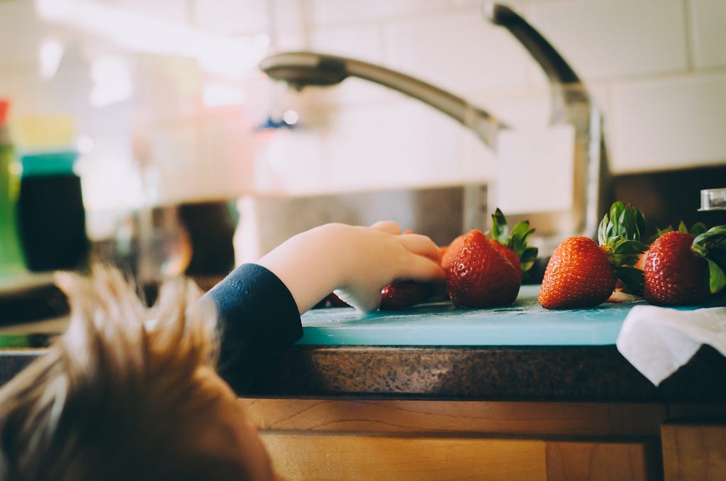 A child reaching up to a counter to take a strawberry