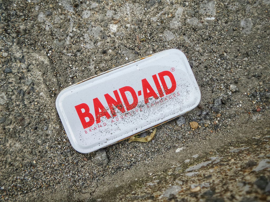 Close up of Band-Aid container resting on concrete ground.