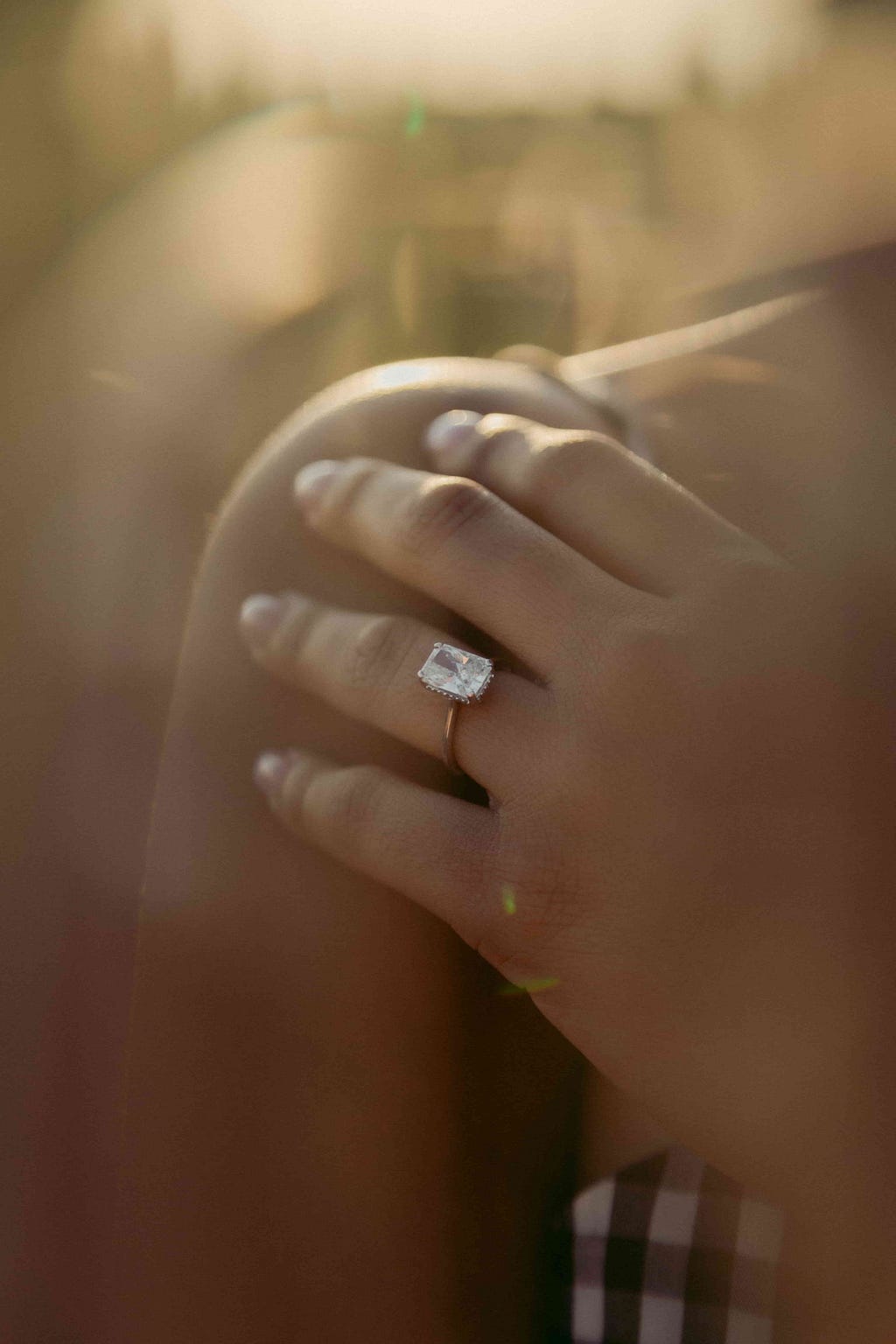 A diamond engagement ring on a woman’s hand which is resting on her shoulder.