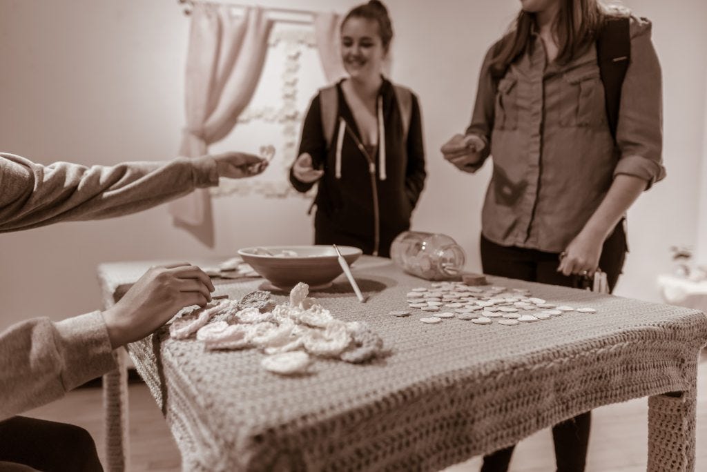 Claudia V. Solorzano handing a crocheted heart to a gallery guest at the Maxine Merlino Gallery at the School of Art at Long Beach State University, December 2018