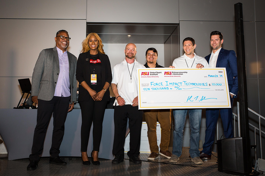 Past venture challenge winners pose with a giant check on a stage at the 2019 Global Sport Summit