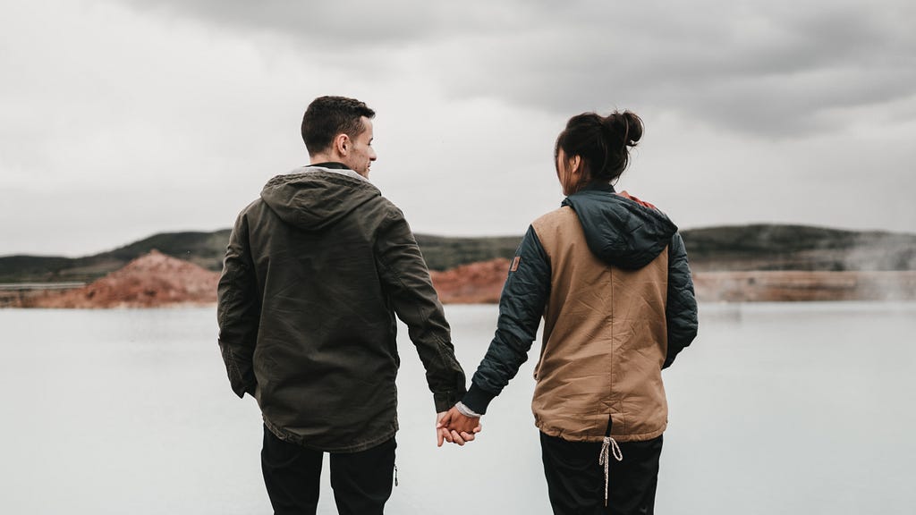 A couple standing at the edge of a cliff holding hands.