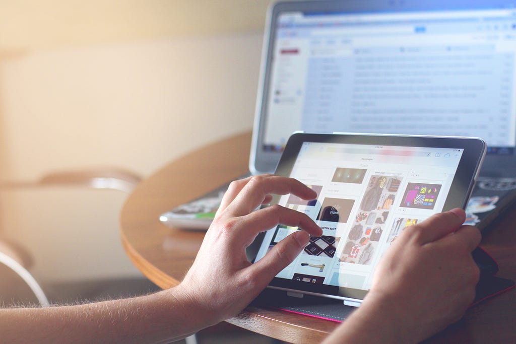 A person using a touch device at their desk with their laptop in the background