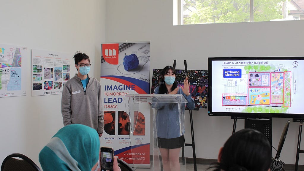 Two students presenting in front of an audience with a TV showing their project.