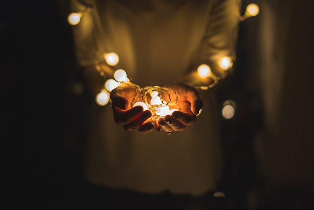 Person holding a string of Christmas lights in their arms and hands