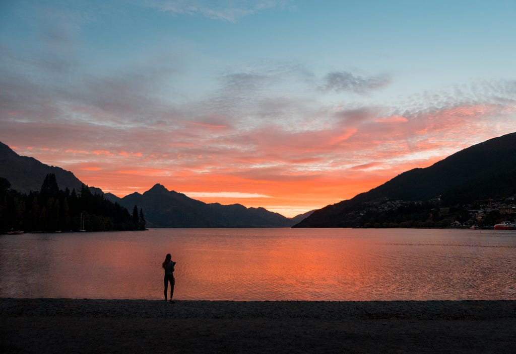 A person watching the sun set over water and mountains