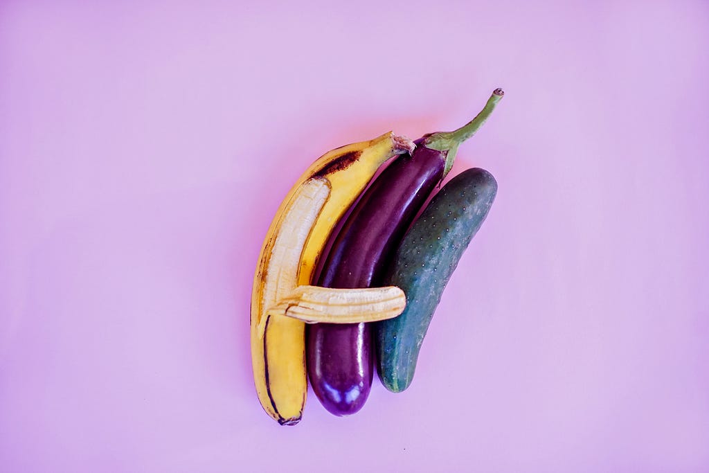 A yellow banana, an eggplant, and a cucumber in a purple background